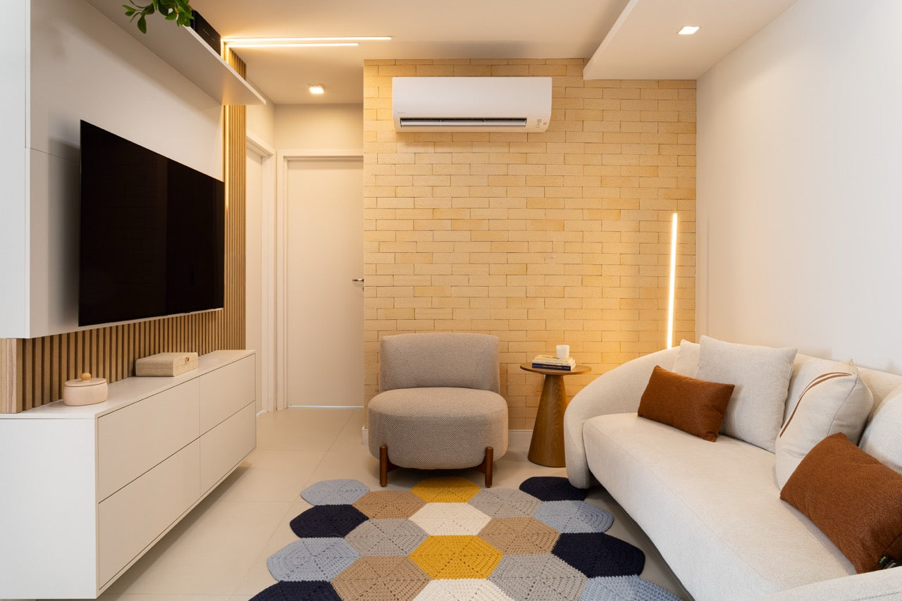 Sala de estar com revestimento de tijolinho decorativo Quarel Rustic Sand na parede de destaque, sofá branco e iluminação quente